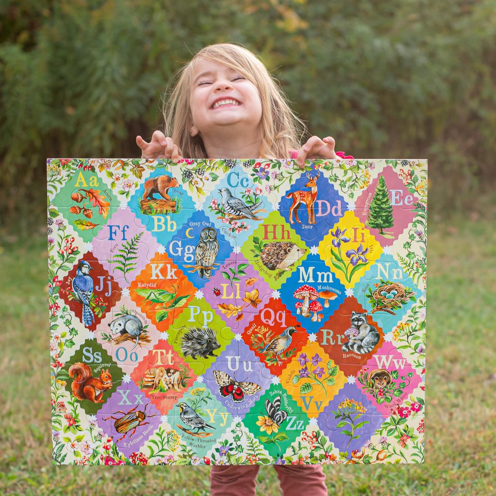 Child holding a colorful alphabet chart outdoors. A is for Acorn 36 Piece Giant Alphabet Puzzle
