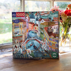 Jigsaw puzzle box with a colorful illustration of a city scene on a wooden surface. Artists in Venice Italy 1000 Piece Puzzle
