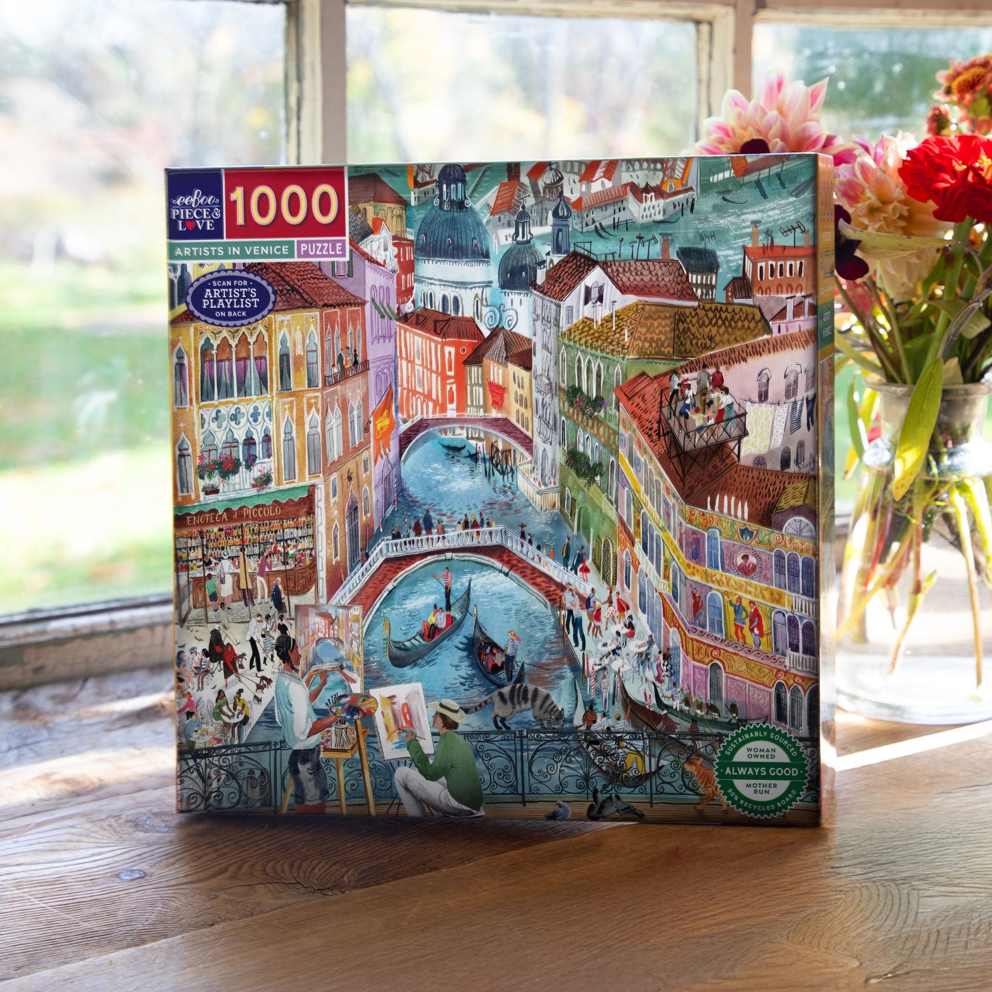 Jigsaw puzzle box with a colorful illustration of a city scene on a wooden surface. Artists in Venice Italy 1000 Piece Puzzle
