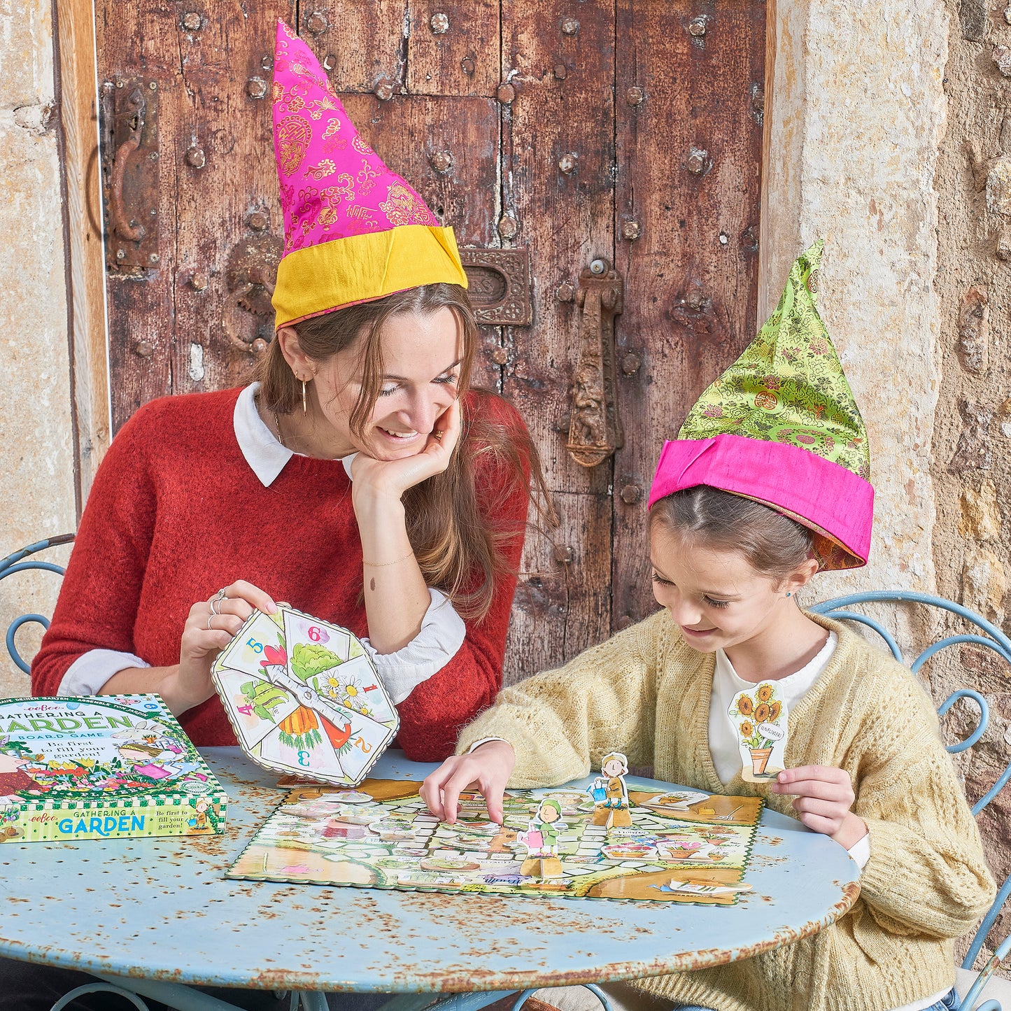 Two people wearing colorful hats playing a board game outdoors. Gathering a Garden | Award Winning Kids Board Game by eeBoo