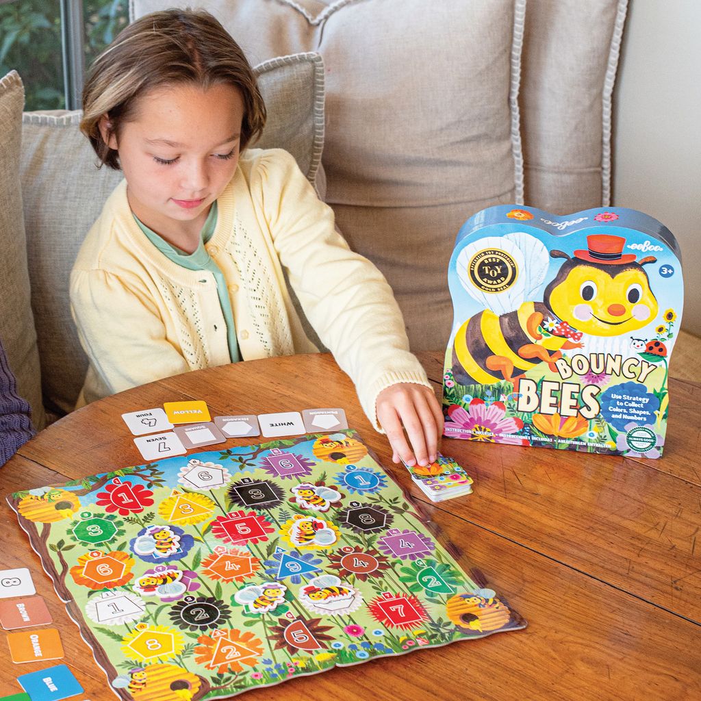 Child playing with a board game titled 'Bouncy Bees' on a wooden table.