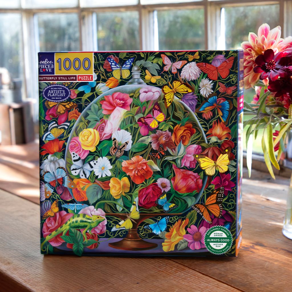 Jigsaw puzzle box with colorful floral and butterfly design on a wooden table. Butterfly Still Life 1000 Piece Puzzle
