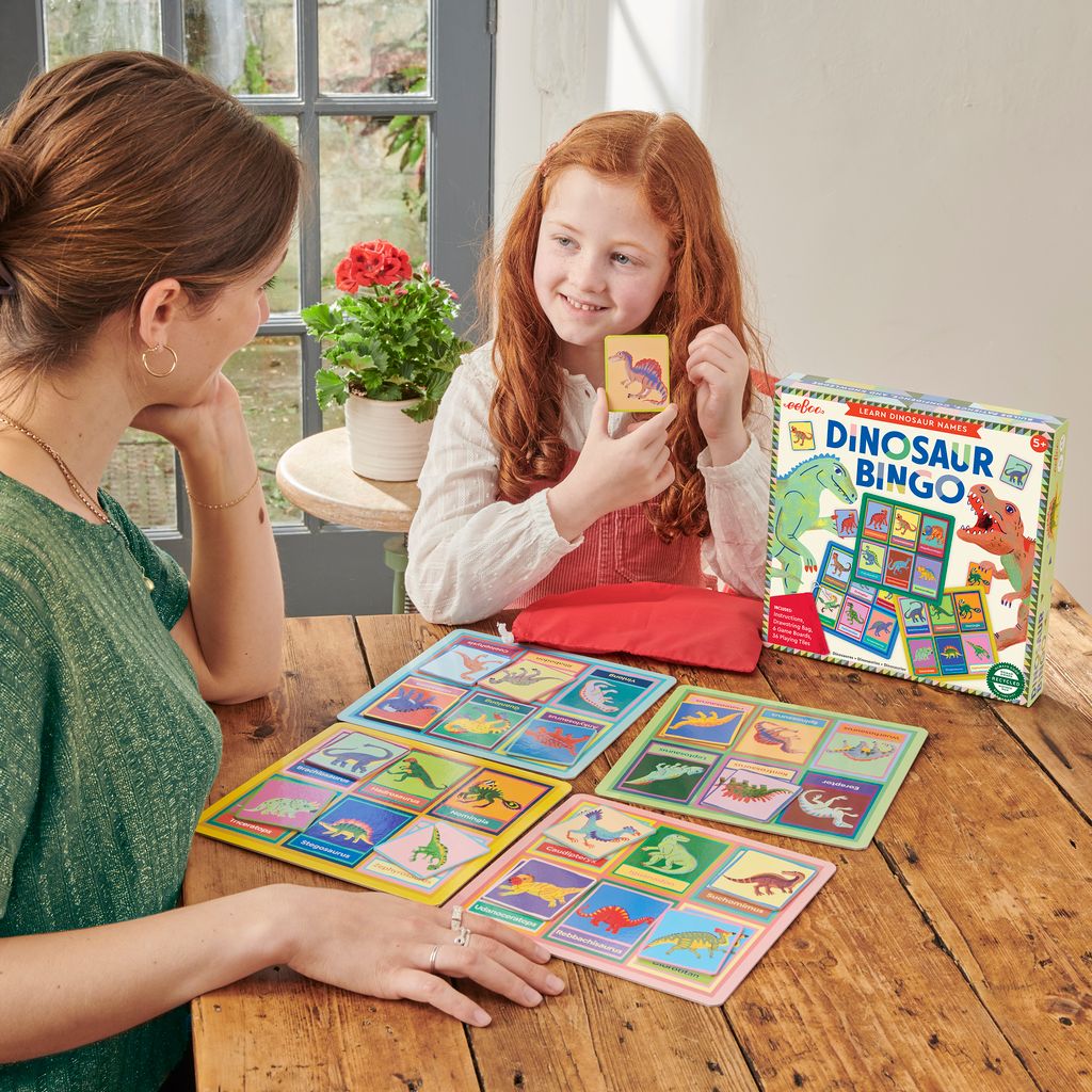 Two people playing a Dinosaur Bingo game at a wooden table.