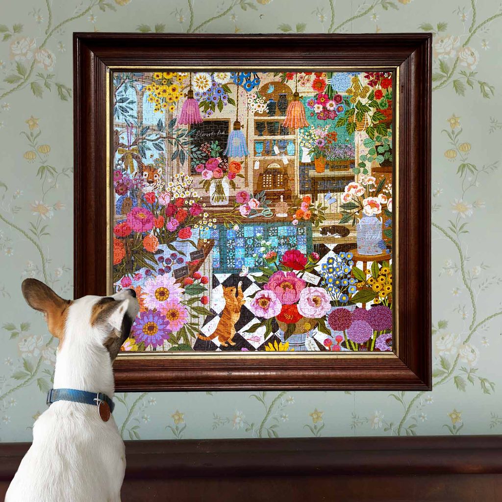 Dog looking at a colorful framed artwork of cats and flowers on a floral wallpapered wall.