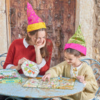 Two people wearing colorful hats playing a board game outdoors. Gathering a Garden | Award Winning Kids Board Game by eeBoo