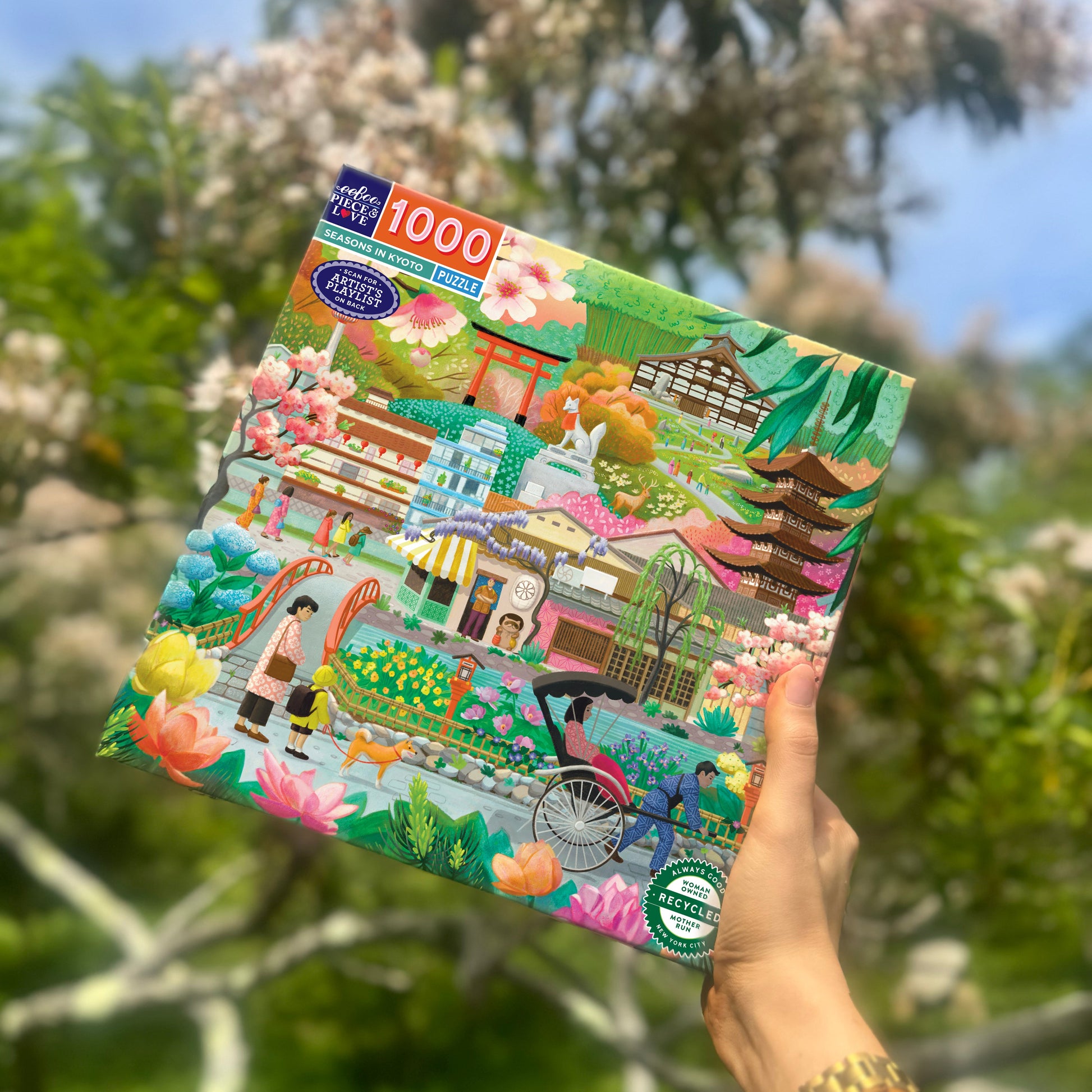 Hand holding a colorful puzzle box with a scenic design against a natural background