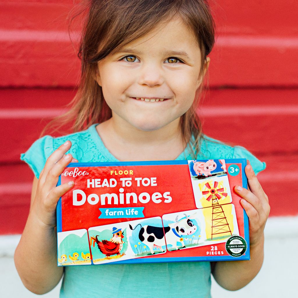 Child holding a 'Head to Toe Dominoes' game box. Little Farm Head to Toe Dominoes