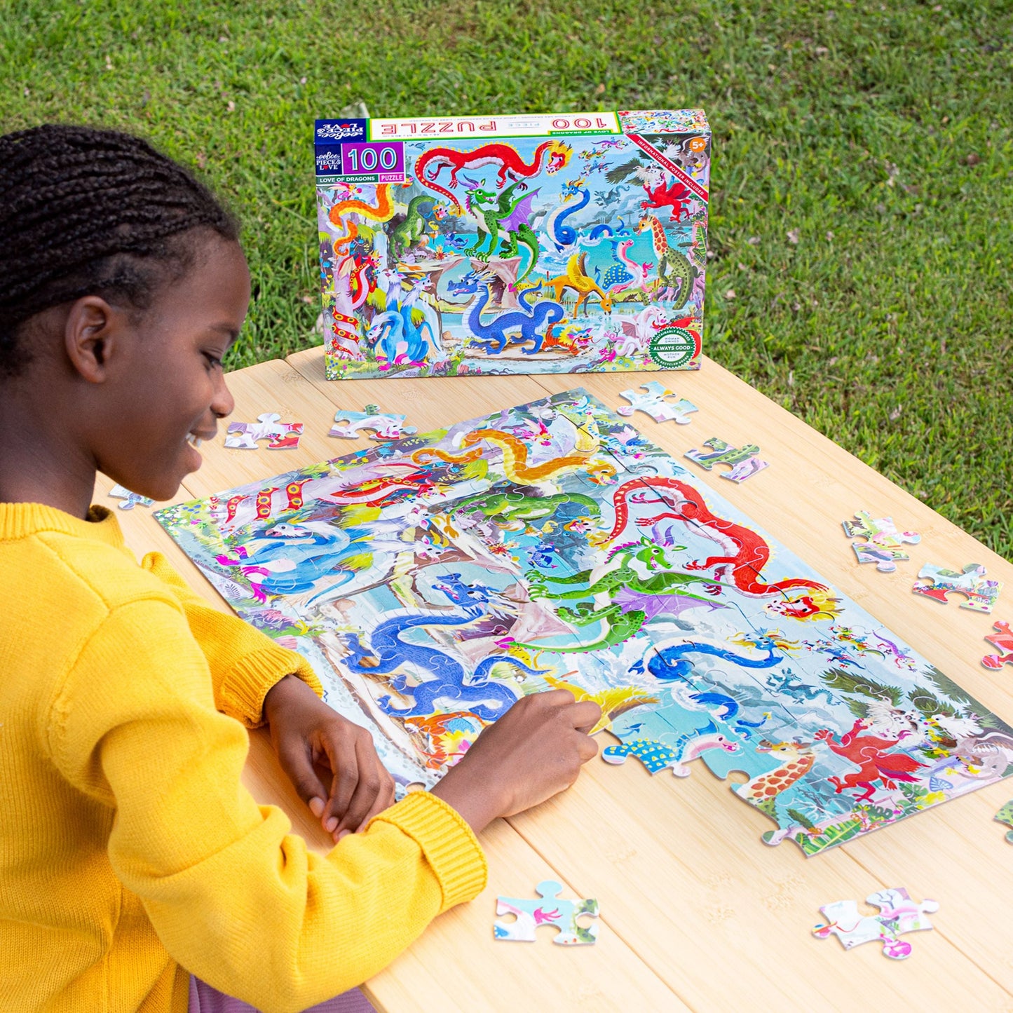 Child playing with a dragon puzzle on a wooden table outdoors. Love of Dragons 100 Piece Puzzle