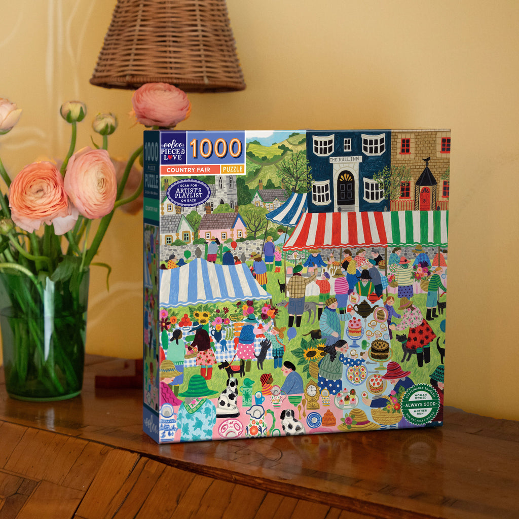 Artist Vanessa Bowman depicts a festive village square filled with tents, crafts & a colorful crowd gathering for the country fair. 1000 Piece Jigsaw Puzzle by eeBoo 