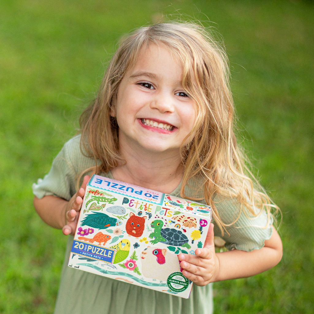 Child holding a puzzle box with a green outdoor background. Petite Pets 20 Piece Puzzle