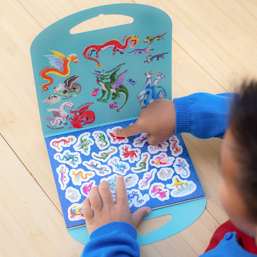 Child interacting with a book of colorful dragon stickers on a wooden floor.