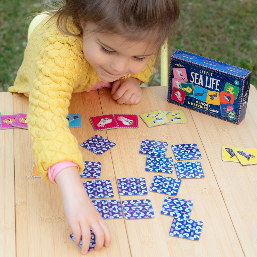 Child playing with a 'Little Sea Life' memory matching game on a wooden table.