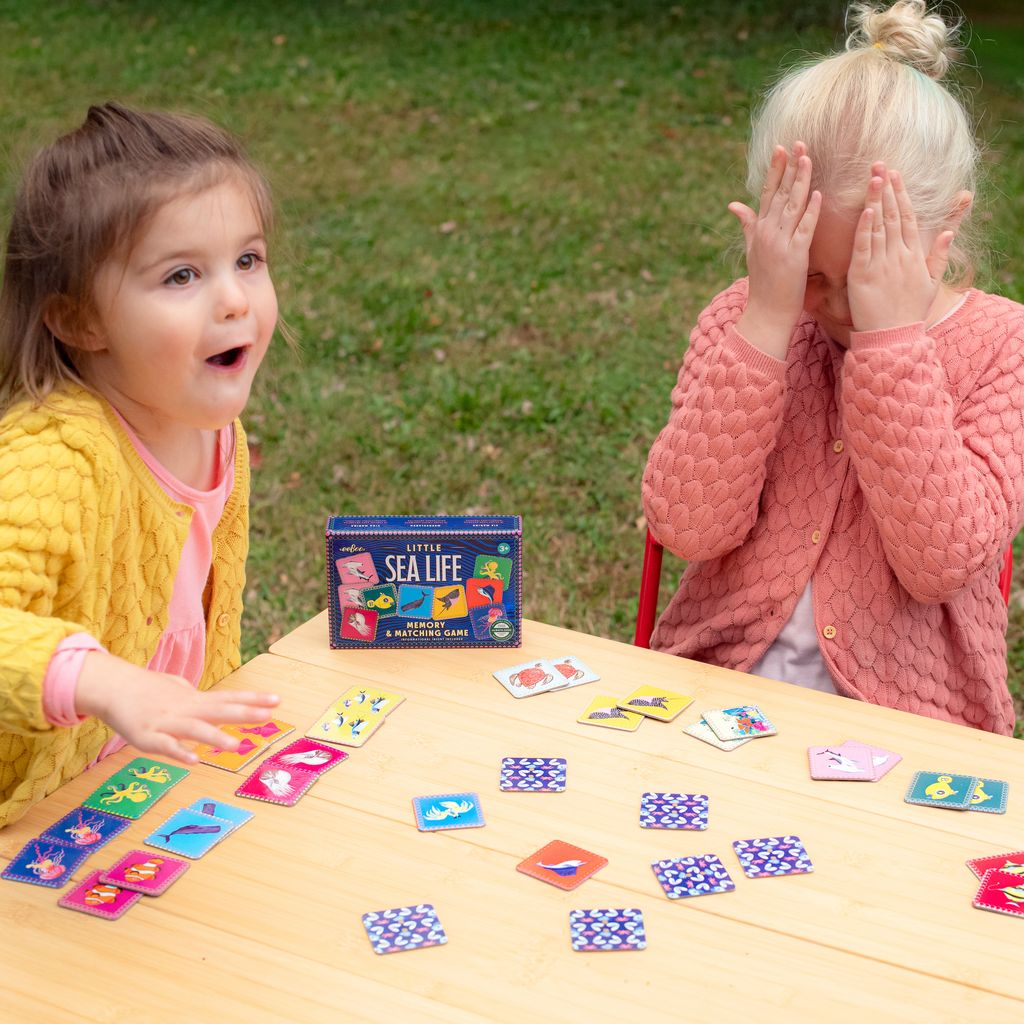 Two children playing with a 'Little Sea Life' card game outdoors.