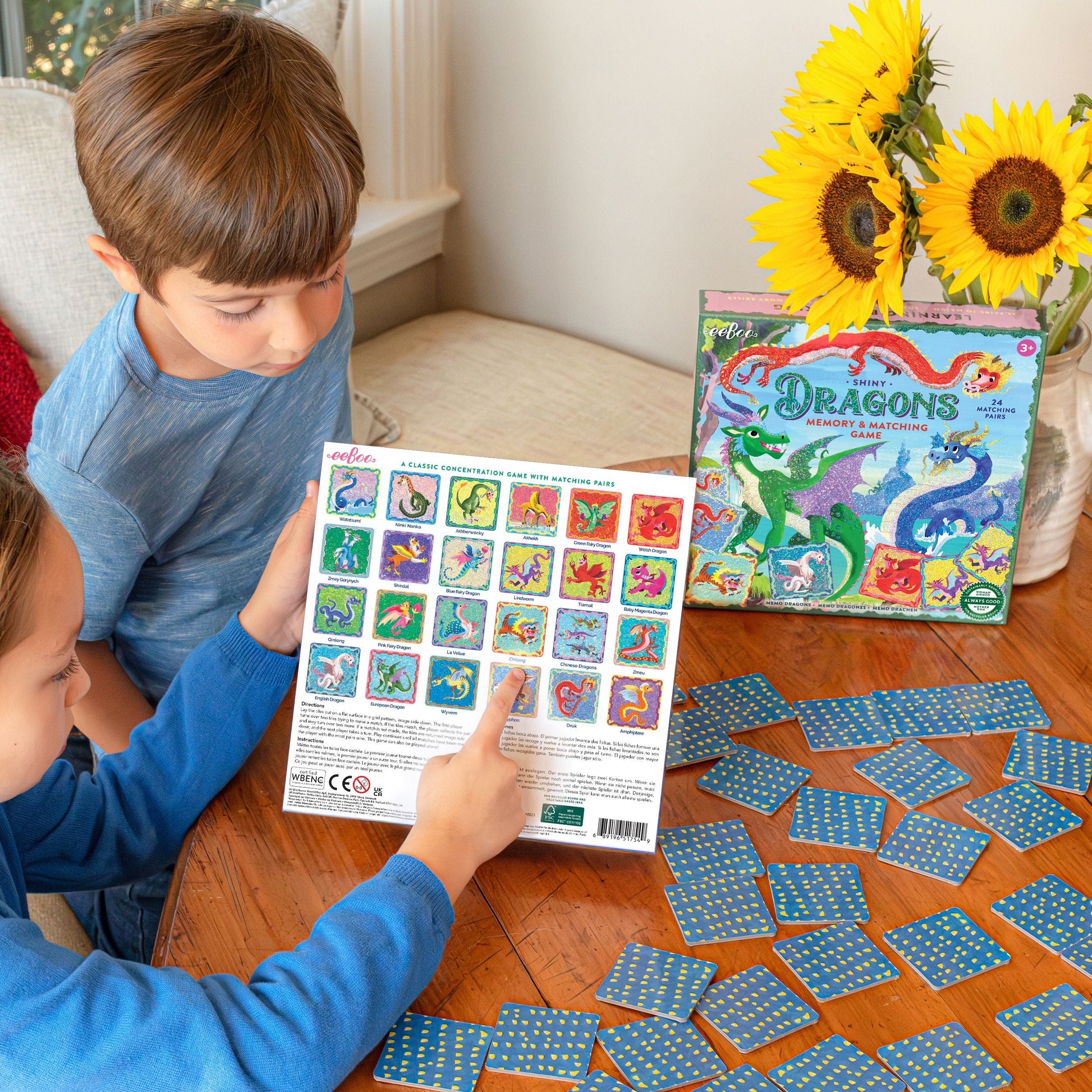 Two children playing with a dragon-themed card game on a wooden table.