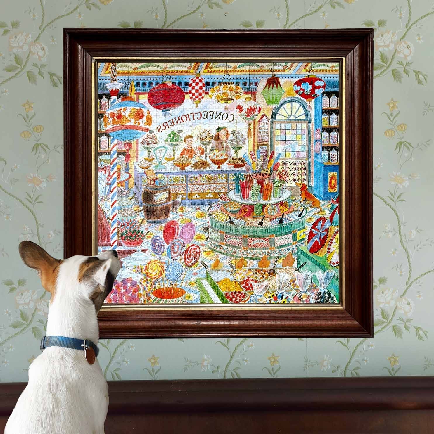 Dog looking at a colorful framed artwork of a candy store on a floral wallpapered wall.