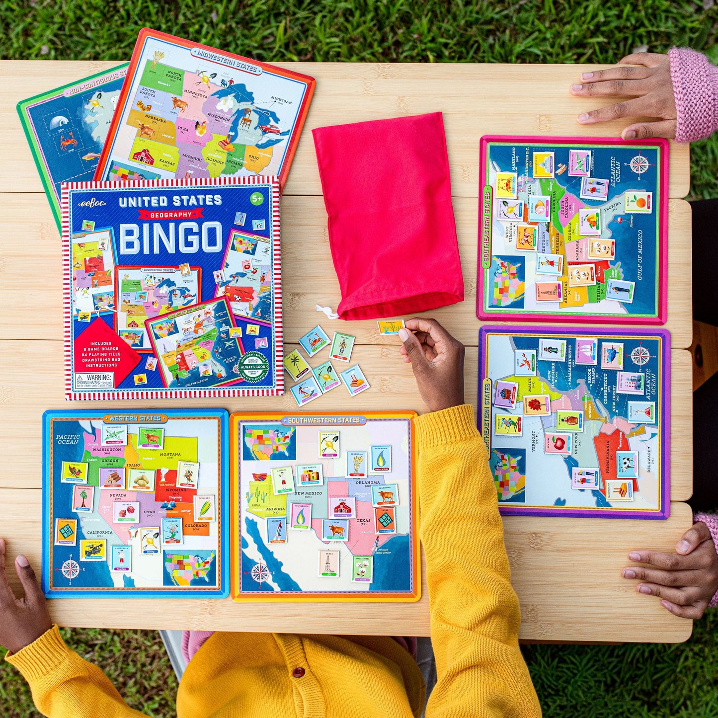 Children playing with a United States Bingo game on a wooden table outdoors.