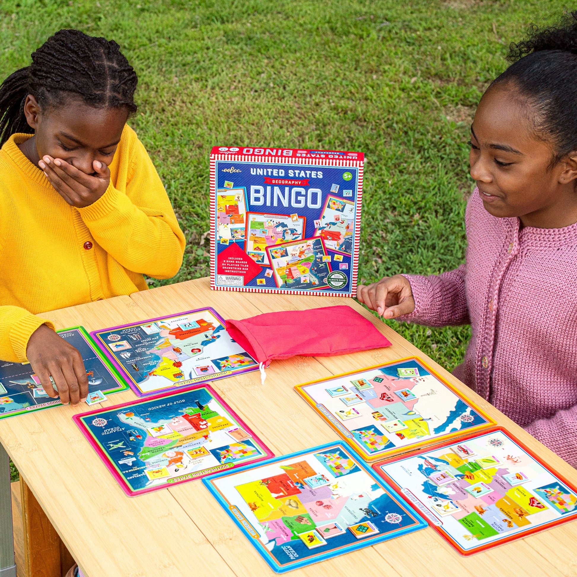 Two children playing with a Bingo game outdoors on a grassy area.