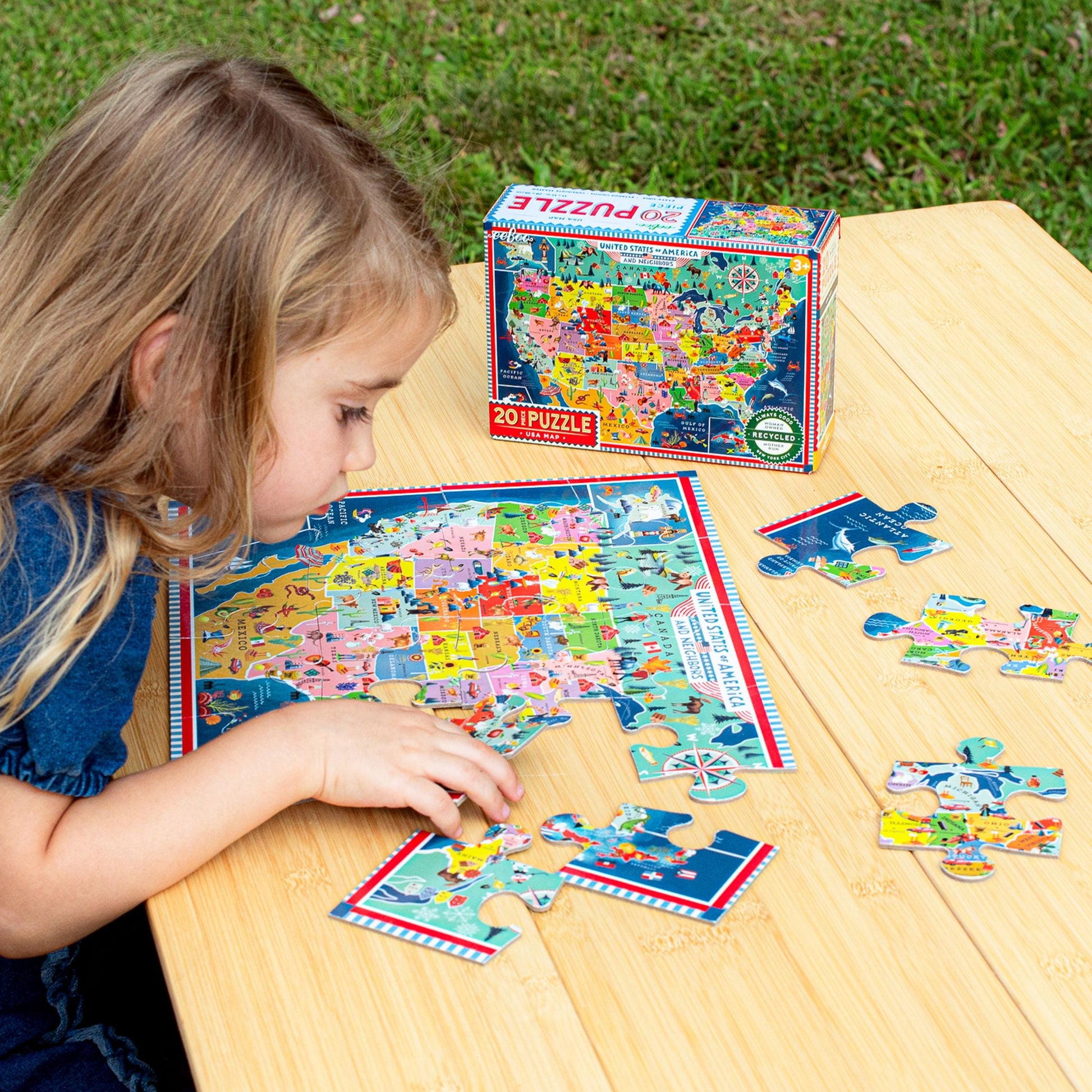 Child playing with a puzzle of the United States on a wooden table outdoors. USA Map 20 Piece Puzzle