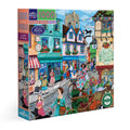 Jigsaw puzzle box featuring a colorful village scene with shops and people. Village by the Sea 1000 Piece Puzzle