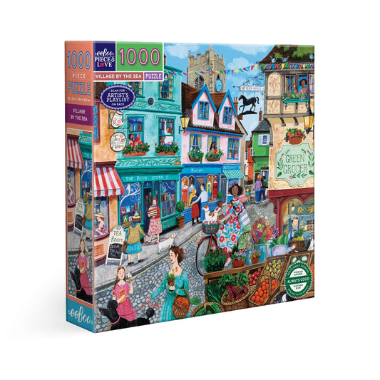 Jigsaw puzzle box featuring a colorful village scene with shops and people. Village by the Sea 1000 Piece Puzzle