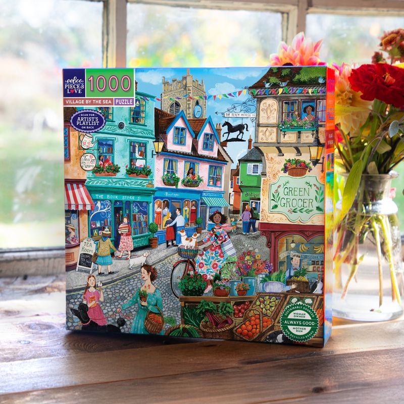 Jigsaw puzzle box with colorful illustration of a village scene on a wooden surface.