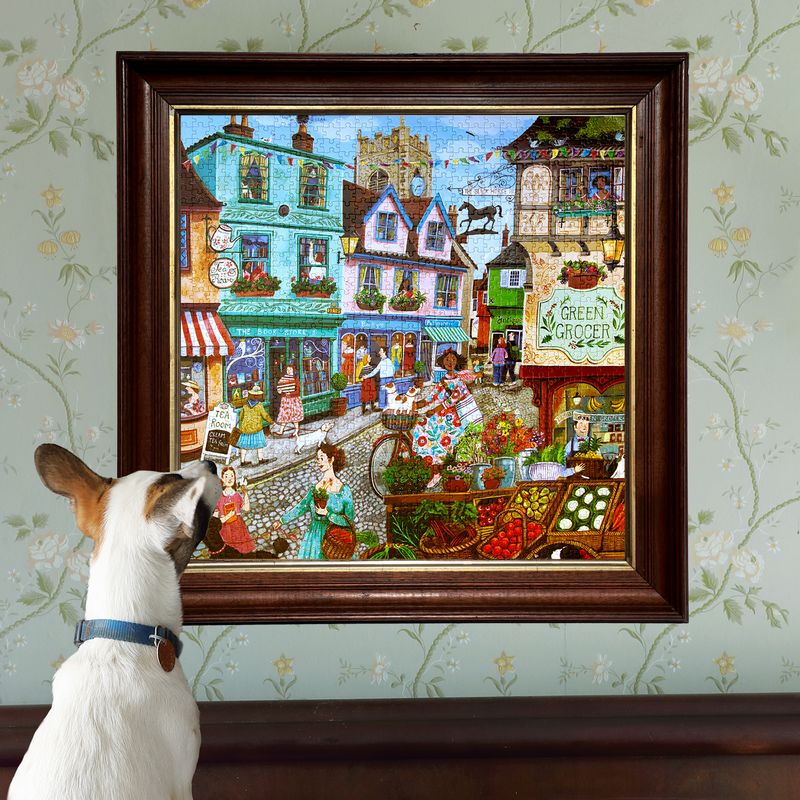Dog looking at a colorful framed painting of a village scene on a wall with floral wallpaper.