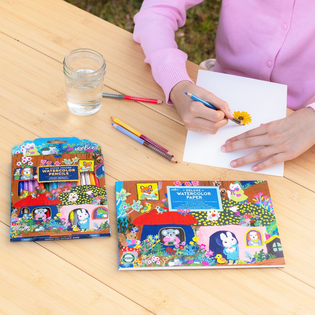 Child drawing with watercolor pencils and paper on a wooden table