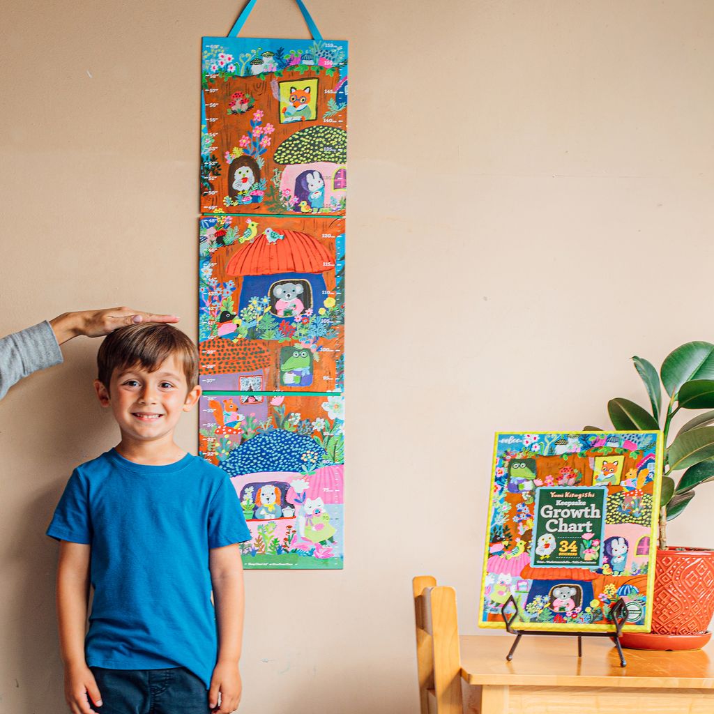 Child standing next to a colorful growth chart on a wall. Yumi Growth Chart