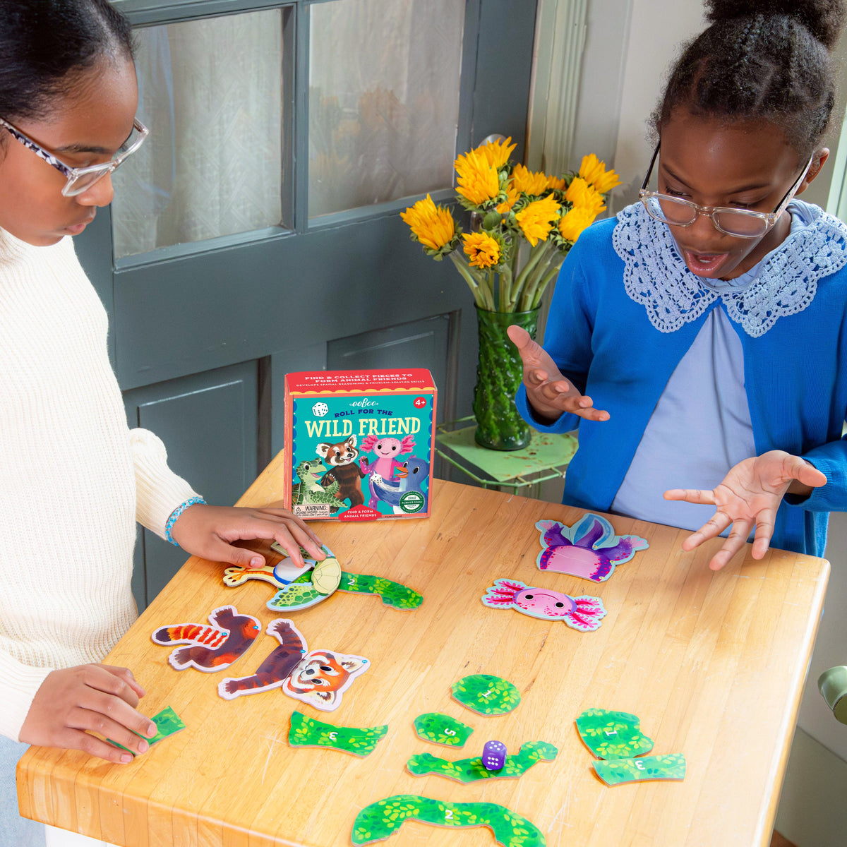 eeBoo Toys & Games: Two children playing with educational toys on a table, with a book titled 'Wild Friend' in the background.