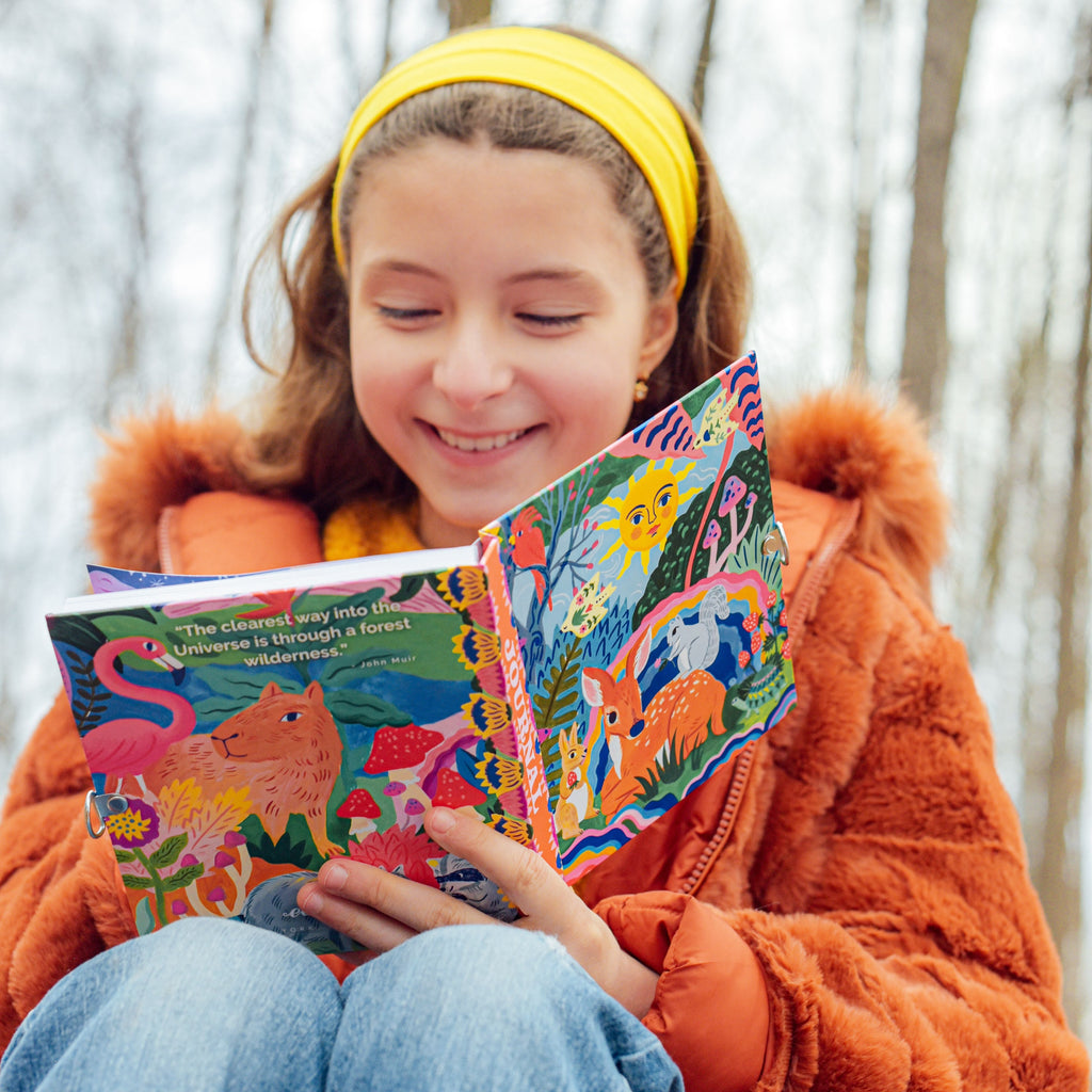 Child with A colorful journal with a whimsical illustration of a deer, rabbit, and various plants.