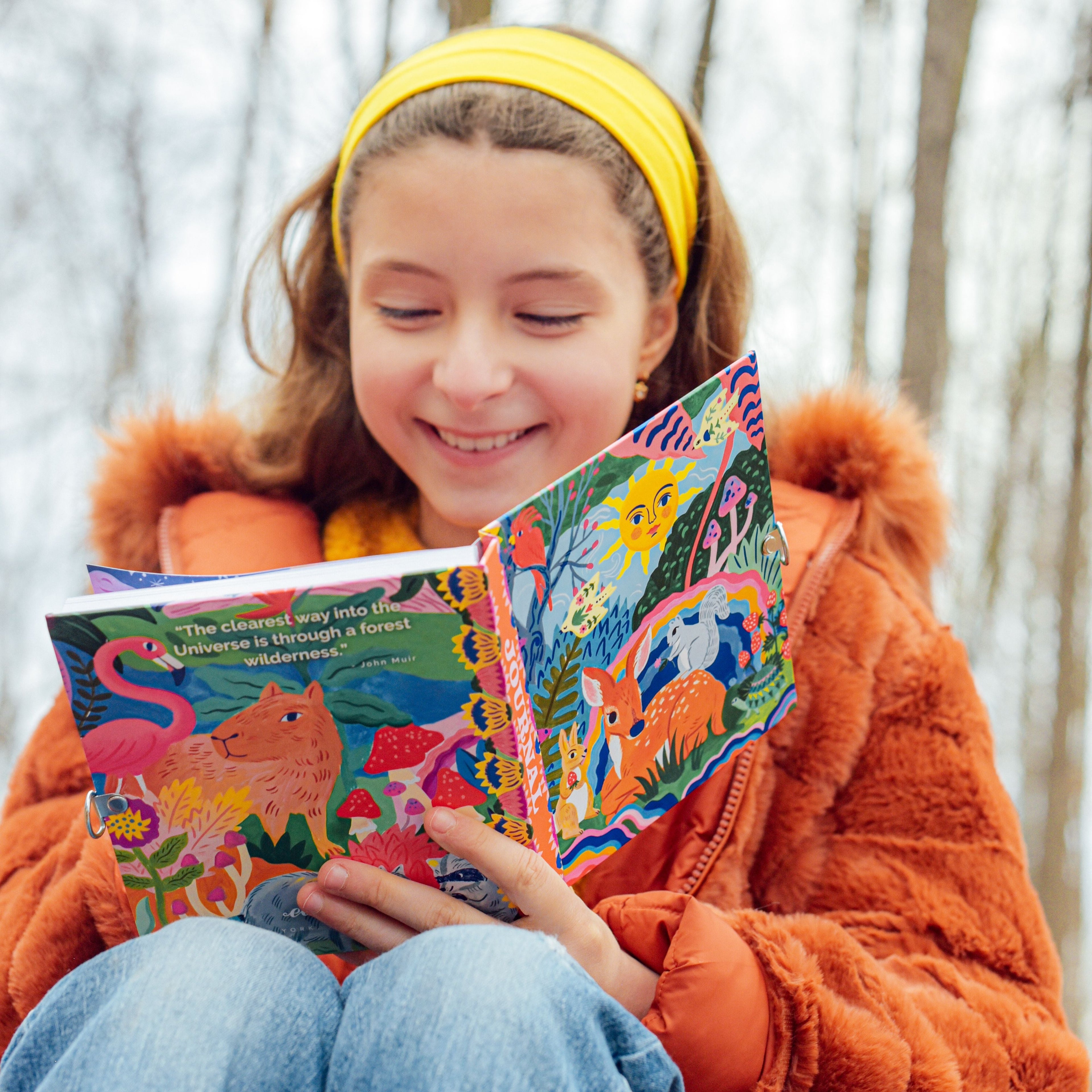 Child with A colorful journal with a whimsical illustration of a deer, rabbit, and various plants.